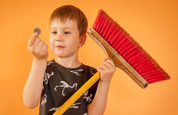 little boy holding a broom in one hand and a quarter in the other